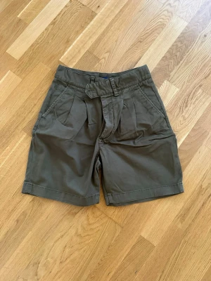 Olivgröna shorts från Gant - Snygga olivgröna shorts från Gant med hög midja . Shortsen har två framfickor, veckade detaljer framtill och stängs med dragkedja. Perfekta för varma dagar och ger en avslappnad men stilren look.