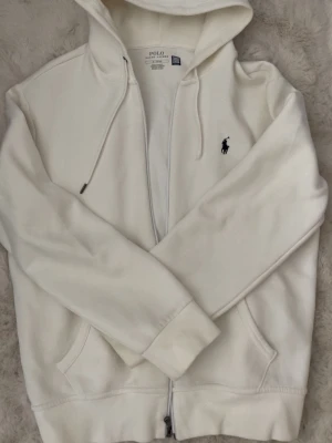 Vit hoodie från Polo Ralph Lauren - vit hoodie från Polo Ralph Lauren med dragkedja, det ena snöret saknar den där grejen längst ner men inget mer är det. 