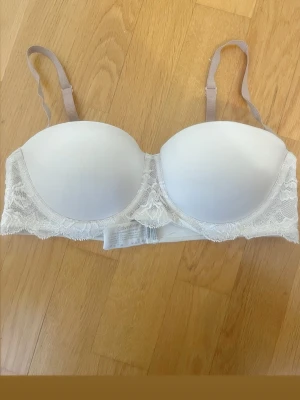 Vit push-up bh från Calvin Klein - Snygg vit push-up bh från Calvin Klein med spetsdetaljer längs kanten. Bh:n har avtagbara axelband och vadderade kupor för extra stöd och form. Perfekt för dig som vill ha en stilren och bekväm bh med en feminin touch.