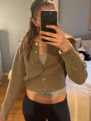 Beige cropped kofta med knappar - Mysig beige kofta i croppad modell med stora knappar framtill. Koftan är stickad och har långa ärmar samt ribbade muddar. Perfekt att slänga över ett linne eller t-shirt för en chill look.