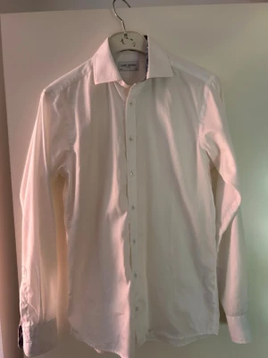 Vit skjorta från John Henric  - Klassisk vit skjorta från John Henric med lång ärm och knappar framtill. Skjortan har en stilren design med normal passform och är tillverkad i bomull. Perfekt för en clean och snygg look.