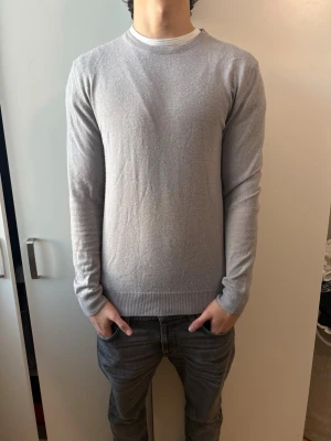 J Lindeberg merinoulltröja  - En stilren ljusgrå stickad tröja med rund halsringning och långa ärmar från J Lindeberg med 100% merinoull, nyskick använd max 5 gånger. Nypris-1300kr mitt pris-500kr. Storlek L men passar som M, pris kan diskuteras vid snabba affärer.