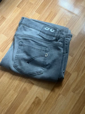 Dondup George  - Snygga grå jeans med en unik broderad detalj på bakfickan och tryckt logga på linningen. Klassisk femficksmodell i mjukt denimtyg, perfekt för en avslappnad stil. Passar dig som gillar stilrena och enkla jeans med en twist.