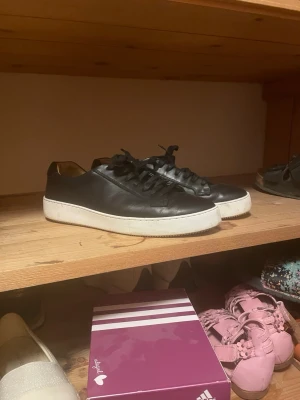 Svarta lädersneakers med vit sula Tiger of Sweden - Stilrena svarta sneakers i läder med klassisk vit sula och svarta skosnören. Låg modell som passar perfekt till streetwear och casual outfits. Enkel och tidlös design som funkar till det mesta. Tiger of Sweden.