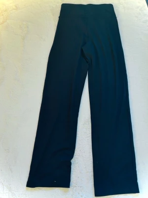 Svarta träningsbyxor - Säljer ett par svarta träningsbyxor med raka ben och hög midja. De är stretchiga och sitter skönt, perfekta för dig som gillar en avslappnad men ändå snygg look. Diskret logga på höften och mjukt material som formar sig efter kroppen.