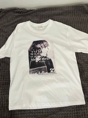 Vit Maison Margiela t-shirt med tryck - Vit t-shirt från Maison Margiela med ett stort grafiskt tryck framtill i svartvitt. Klassisk rund halsringning och korta ärmar. T-shirten har en avslappnad passform och är tillverkad i mjuk bomull.
