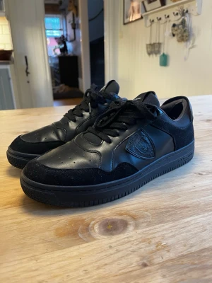 Svarta sneakers från Philippe Model - Stilrena svarta sneakers från Philippe Model med lågt skaft. Skorna har en mix av slätt läder och mockadetaljer, svarta skosnören och diskret logga på sidan. Perfekta för dig som gillar en clean och modern look. Hål i hälarna på båda skorna men det sitter ”Laglappar” så de märks inte över huvudtaget. Storlek 44. Pris är inte hugget i sten