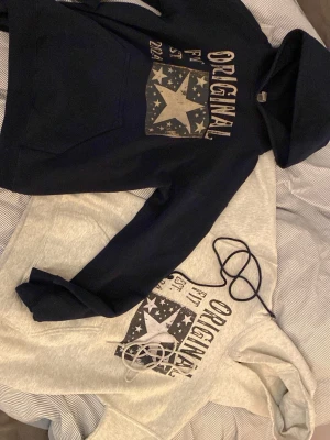 Två hoodies med stjärntryck - Två hoodies i olika färger, en svart och en ljusgrå, båda med trycket 'ORIGINAL' och en stor stjärna framtill. Klassisk huva och magficka. Perfekta för en avslappnad stil.