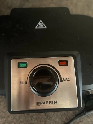 Svart våffeljärn Severin - Ett svart våffeljärn från Severin med justerbar temperatur och indikatorlampor. Järnet har plats för två hjärtformade våfflor åt gången och är tillverkat i metall och plast. Perfekt för att snabbt fixa frasiga våfflor hemma.