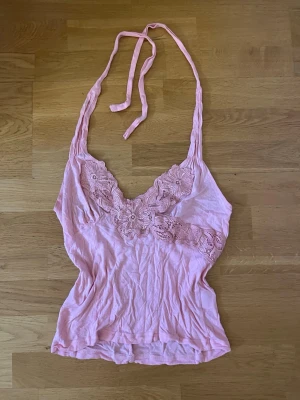 Rosa halterneck linne med spetsdetaljer - Söt ljusrosa linnetopp med knyt i nacken och v-ringad hals. Toppen har fina spetsdetaljer med blommönster över bysten som ger en romantisk känsla. Sitter jättefint och passar till sommaren! 