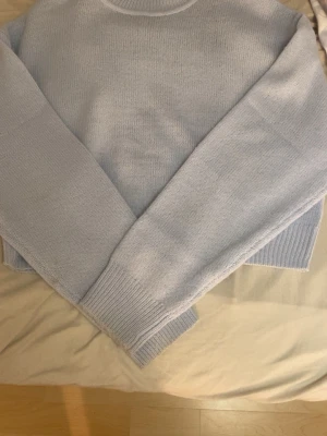 Ljusblå cropped stickad tröja - Säljer en ljusblå cropped stickad tröja med rund hals och långa ärmar. Tröjan har ribbade muddar vid ärmslut och nederkant, vilket ger en snygg och avslappnad look. Perfekt att matcha med höga jeans eller kjol.