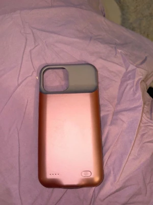 Rosa batteriskal till iPhone - Snyggt rosa mobilskal med inbyggt batteri och grått övre parti. Skalet har en power-knapp och LED-indikatorer för batterinivå. Passar iPhone med stor kameraöppning. Perfekt för dig som vill ha extra batteritid och stilren look. För en iPhone 13