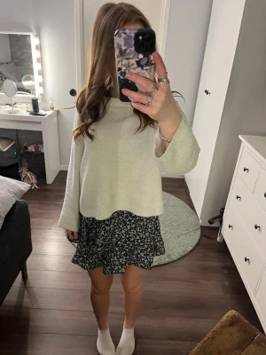 Svart blommig kortkjol med volang - Supersöt svart kortkjol med vitt blommönster och volangkant. Kjolen har en flowy passform och är perfekt för dig som gillar en avslappnad men trendig stil. Tillverkad i ett lätt och mjukt material som känns skönt mot huden.