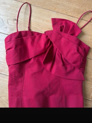 Vinröd linnetopp med rosett - Trendig röd topp med tunna axelband och en dekorativ rosett framtill. Toppen är lite cropped och har dragkedja i ryggen för enkel på- och avtagning. Perfekt till sommaren!! Sitter perfekt! Aldrig använd av mig men tidigare ägaren sydde på ett av banden som gick av, men inget man tänker på. Annars inga defekter, och är från other stories . OBS! För snabb leverans välj PostNord! 