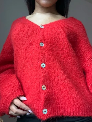 Röd oversized stickad kofta - Helt ny mysig röd kofta med v-ringning och stora pärlemorknappar. Koftan har en oversized passform, långa ärmar och är stickad i ett fluffigt material som känns riktigt skönt. Perfekt att slänga på sig för en chill look.