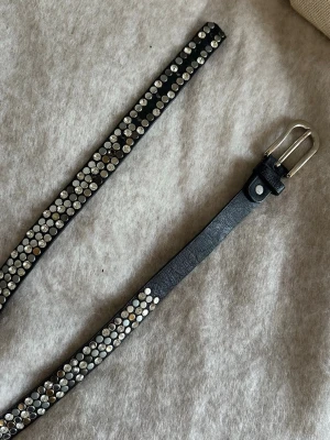 Svart bälte med nitar och strass - Snyggt svart bälte i skinn med tätt placerade silverfärgade nitar och glittrande strassdetaljer längs hela bandet. Från tessie🪩🪩