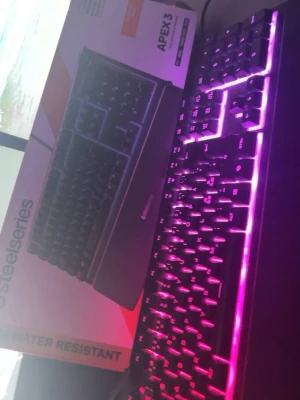 SteelSeries Apex 3 RGB-tangentbord - SteelSeries Apex 3 är ett svart gamingtangentbord med RGB-belysning som lyser i flera färger. Tangentbordet har en klassisk rektangulär form och är tillverkat i plast. Perfekt för gaming och datoranvändning med snygg ljuseffekt.