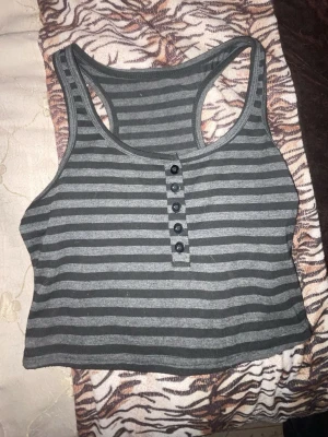 Grå och svart randig croppad linnetopp från Romwe - Säljer en croppad linnetopp i grått och svart med horisontella ränder. Toppen har knappar framtill och breda axelband i brottarryggsmodell. Perfekt till jeans eller shorts för en chill look. Köpt på SHEIN. 