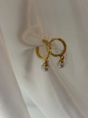 Guldiga hoops med pärlor - Snygga örhängen i guldpläterad med små vita pärlor som hänger ned. Klassisk hoop-modell med en modern twist tack vare pärldetaljen. Perfekta för att lyfta vilken outfit som helst.