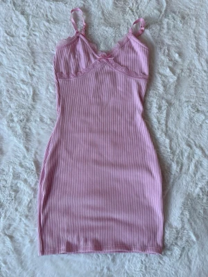 Rosa miniklänning med spets - Rosa figurnära miniklänning med smala axelband, ribbad struktur och spetsdetaljer vid urringningen. Storlek XS, använd en gång. 