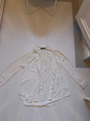 Vit långärmad skjorta med knappar - Klassisk vit skjorta med lång ärm och knappar framtill. Skjortan har en avslappnad passform och lätt rundad nederkant. Perfekt att styla lager på lager eller bära som den är. Tillverkad i mjukt tyg för en bekväm känsla.