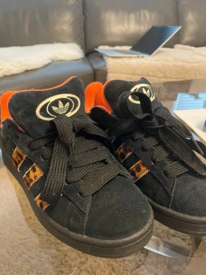 Adidas campus 00s leopard  - Svarta Adidas sneakers i mocka med leopardmönstrade ränder och orange foder. Klassisk modell med svarta snören och svart sula. Använda men i nyskick. Kommer med både svarta och extra vita och oanvända original skosnören.