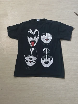 Svart KISS band-tshirt med tryck - Cool svart t-shirt med stort tryck av KISS-medlemmarnas ansikten på framsidan och turnétryck på baksidan. Klassisk passform och rund hals. Perfekt för dig som älskar rock och vill sticka ut med en ikonisk bandtröja.
