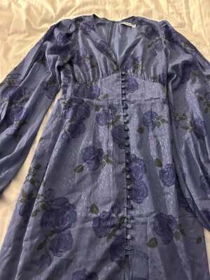Blommig blå långklänning från Adoore - Säljer en elegant blå långklänning från Adoore med blommigt mönster i lila toner. Använd två gånger och är som ny