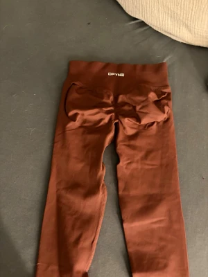 DFYNE Seamless Scrunch Leggings - Brun - Storlek XS - Säljer mina superpopulära DFYNE seamless leggings i en jättefin brun färg. De är i storlek Extra Small (XS) och passar perfekt för gymmet! Dessa tights har den välkända och smickrande scrunch butt-designen (som syns tydligt på bild 1). Materialet är DFYNEs klassiska mjuka, stretchiga och helt knäböjssäkera (squat-proof) tyg. Hög midja som sitter bekvämt på plats. De är i mycket fint skick och säljes då jag rensar ut min samling. Passa på att knipa dessa favoriter! • Märke: DFYNE • Färg: Brun 