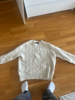 Vit kabelstickad tröja - Säljer en vit kabelstickad Ralph lauren tröja med klassiskt flätmönster framtill och ribbade muddar vid ärmslut och nederkant. Tröjan har rund halsringning och är perfekt för dig som gillar en clean och tidlös stil. Anledningen till att jag säljer är att den är lite för bred för mig i passformen. Den är XL men har krympt lite i tvätten vilken gör att den sitter som M😊 hör av er vid funderingar 