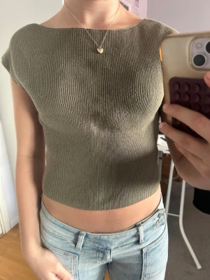 Grön ribbad croppad topp - Säljer en olivgrön ribbad topp med korta ärmar och rund hals. Toppen är i ett mjukt material och har även en fin v-ringning i ryggen. Perfekt till jeans eller kjol! Storlek 158/164 men passar xs. Använd ett fåtal gånger 