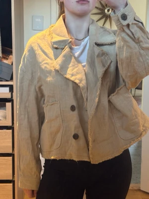 Beige linnejacka med råa kanter - Säljer en beige jacka i linne med råa, fransiga kanter och stora slag. Jackan har dubbelknäppning med två knappar framtill och en avslappnad, loose passform. Perfekt för dig som gillar en chill och trendig look. 😃😍🩷