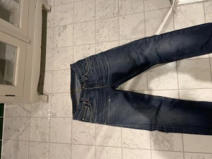 Archive Nudie Jeans & CO - Säljer ett par mörkblå jeans från nudie. Hemma gjorda feta slitningar på bakfickorna. Modellen är mjuk och skön. Sjukt feta fades som är helt gjorda över tiden.