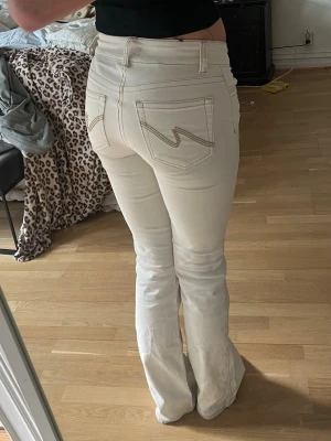 Vita bootcut jeans från Nelly  - Säljer ett par vit/beiga bootcut jeans från Nelly med klassiska bakfickor och beige sömmar. Jeansen har låg midja o dubbla knappar. Finns tecken på användning längst ner på jeansen och pyttelitet märke på baksidalår😊kontakta vid frågor eller köp direkt💞