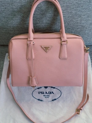 Saffino läder Prada väska - Underbart fin Prada väska i saffino läder inköpt i Stockholm säljes då den tyvärr ej används tillräckligt. Fin rosa färg och kan bäras på olika sätt. Axelrem och fina handtag. Har några mindre skavanker men i fint skick. Kommer med dustbag. Saffion läder är tåligare och eftertraktat. Om du vill införskaffa en superfin vår/sommar väska slå till för ett toppen pris 🌺   Mått:  Längd 31cm Höjd 24cm Bredd 13cm