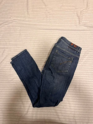 Blå jeans från dondup George med slitningar - Säljer ett par klassiska blå jeans från dondup George med raka ben och femficksmodell. Jeansen har snygga detaljer på bakfickorna och en brun patch med logga i midjan. Tillverkade i slitstark denim som passar perfekt till din vardagsstil. Ställ frågor om ni undrar nått jag fraktar direkt✅