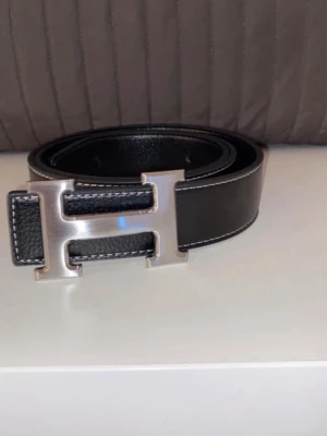 Svart skärp med H-spänne  - Snyggt svart skärp  med stort H-format metallspänne i silverfärg. Nyskick med snabb frakt! Hör av vid frågor.