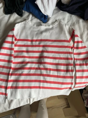 Vit och röd randig tröja Hampton Republic - Säljer en vit långärmad tröja från Hampton Republic med röda horisontella ränder. Tröjan har rund halsringning och är tillverkad i ett mjukt, ribbat material. Perfekt för en avslappnad och stilren look.