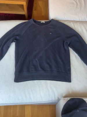 Mörkblå sweatshirt från Acne Studios - En stilren mörkblå sweatshirt från Acne Studios med rund halsringning och diskret logotyp på bröstet. Tröjan har långa ärmar och mjukt material som känns skönt mot huden. Perfekt för en avslappnad och trendig look. Använd fåtal gånger. Den är även vintage så först till kvarn!