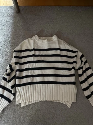 Randig stickad tröja från Guess - Snygg stickad tröja från Guess i vitt med svarta horisontella ränder. Den är väldigt luftigt material som är perfekt för sommar. Orginalpris 600kr 