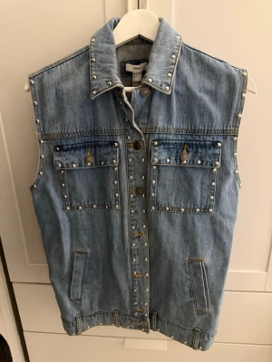 Ljusblå jeansväst med nitar Zara - Säljer en ljusblå oversized jeansväst från Forever 21 med coola silverfärgade nitar längs kanterna och fickorna. Västen har två bröstfickor med knappar och två sidofickor. Klassisk krage och knappstängning framtill. 