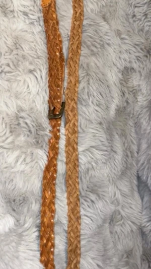 Flätat brunt bälte i skinn - Snyggt flätat bälte i brunt skinn med klassiskt spänne i metall. Perfekt accessoar för att lyfta din outfit och funkar till både jeans och klänning. Bältet har en tidlös design och är lätt att justera i längden.