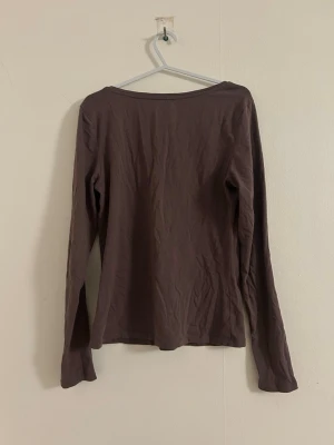 Brun långärmad topp i bomull - En enkel brun långärmad topp med rund halsringning. Tillverkad i mjuk bomull, perfekt för lager på lager eller att bära som den är. Stilren och basic design utan detaljer.