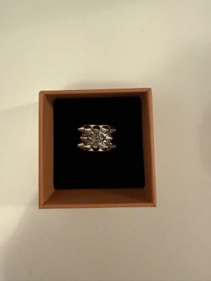 Bred silverfärgad ring med nitar - Snygg bred ring i silverfärg med nitar. Ringen har en modern och unik design som sticker ut och passar perfekt för dig som gillar statement-smycken. Tillverkad i metall.