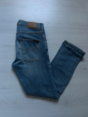 Ljusblå nudie jeans - Authentic Nudie Jeans Lean Dean model in light wash denim, size 28/30, purchased in Gothenburg. These jeans offer a slim fit, showing some wear with fading and subtle distressing adding to their unique character. Please refer to photos for specific details, as these are pre-owned. Feel free to ask any questions! If you wonder about the size if it will fit you tell me your height and weight and I tell you if it fits you!