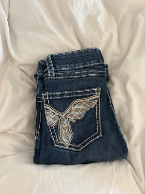 Mörkblå bootcut jeans - Snygga mörkblå jeans med bootcut-modell och dekorativ brodyr med paljetter på bakfickan. Jeansen har kontrastsömmar och klassisk femficksdesign.