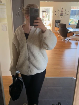 Piléjacka från Lindex - Mysig slutsåld teddyjacka från Lindex med dragkedja framtill och två snedställda fickor. Jackan har ribbade muddar vid ärmslut, hals och nederkant. Perfekt för att hålla sig varm och snygg under kyliga dagar. För referens är jag 176 cm.