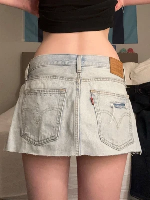 Levi's ljusblå jeanskjol kort modell - Trendig ljusblå jeanskjol från Levi's i kort modell med rå kant nertill. Kjolen har klassiska fem fickor, slitningar framtill och Levi's ikoniska läderpatch bak i midjan. Perfekt för dig som gillar en avslappnad och cool stil. 39cm raktöver midjan❤️