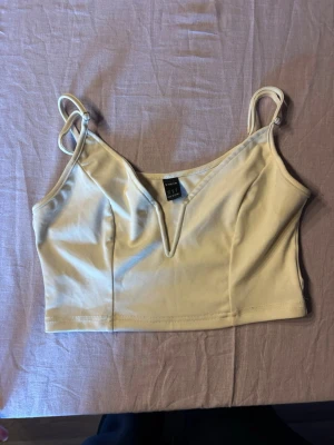 Beige croppad linnetopp med v-ringning - Snygg beige croppad linnetopp från Bik Bok med smala axelband och v-ringad detalj framtill. Tillverkad i mjukt syntetmaterial som sitter skönt mot kroppen. Perfekt att styla med höga jeans eller kjol.