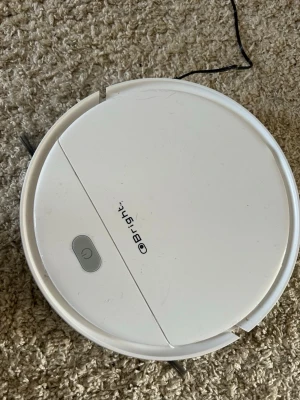 Obright vit robotdammsugare - Smart vit robotdammsugare från Obright med rund form och enkel knapp på ovansidan. Den har borstarmar för effektiv rengöring och är tillverkad i plast. Perfekt för automatiserad städning av hemmet.